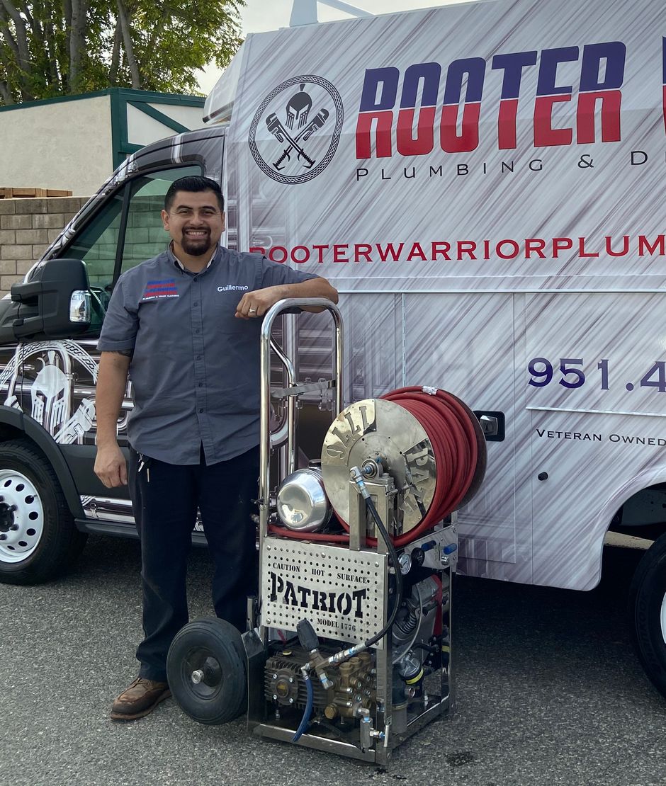 Guillermo of Rooter Warrior standing beside the Patriot jetter and a branded service truck