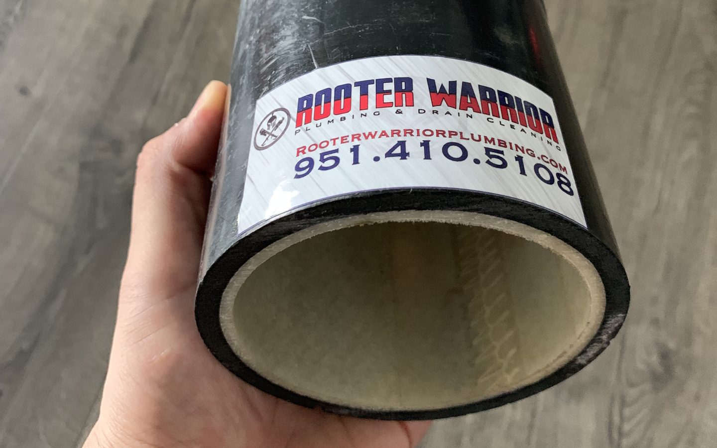 Cut section of an old pipe with a new liner cured inside it, labeled with a Rooter Warrior sticker